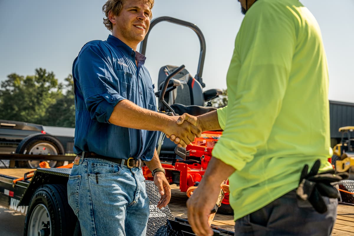 salesman and customer shaking hands in front of kubota mower